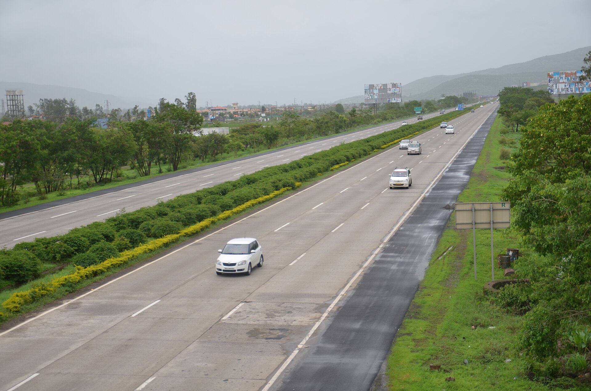 Cars on the wide, divided Mumbai–Pune Expressway on a grey monsoon morning, green hills in the distance