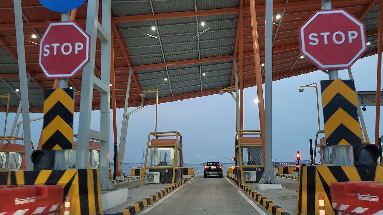 A car approaching a toll plaza lane with red STOP signs and yellow-and-black barriers at dusk