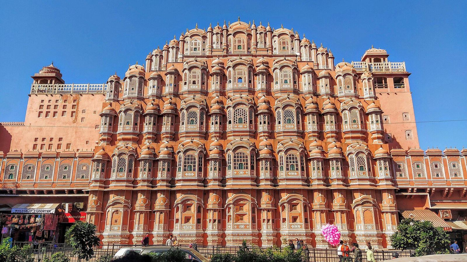 The pink sandstone Hawa Mahal in Jaipur under a bright blue sky, with market stalls at street level