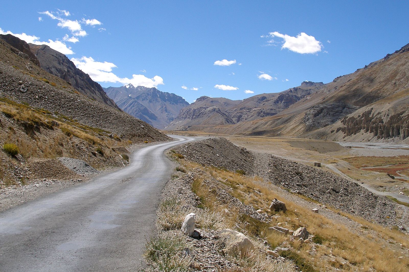 A narrow road winding along a bare mountain valley on the Leh–Manali Highway under a blue sky